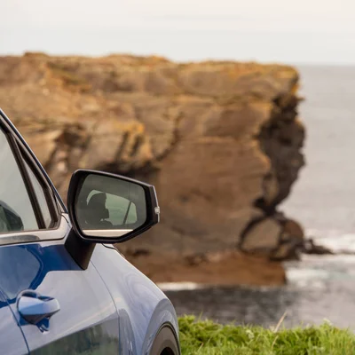 A Blue Car Is Parked On The Side Of A Road Next To A Cliff Overlooking The Ocean In West Ireland