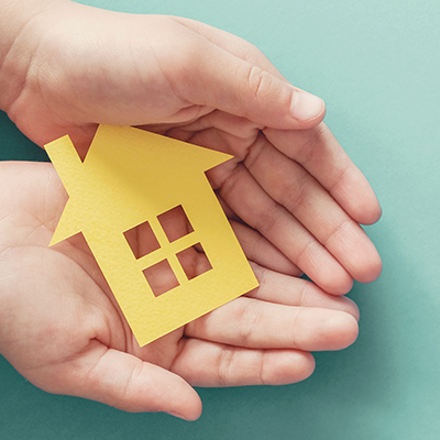 Hands Holding Yellow Paper House Representing Home Insurance With A Blue Background