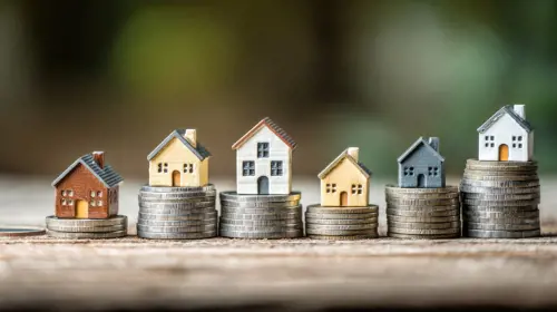 A row of miniature houses on a wooden surface, with a blurred green background.