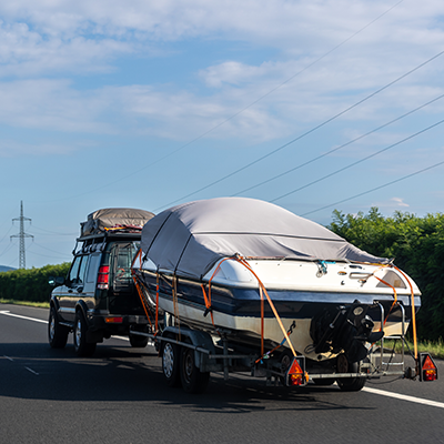 Black Car Towing A Boat Along A Main Road