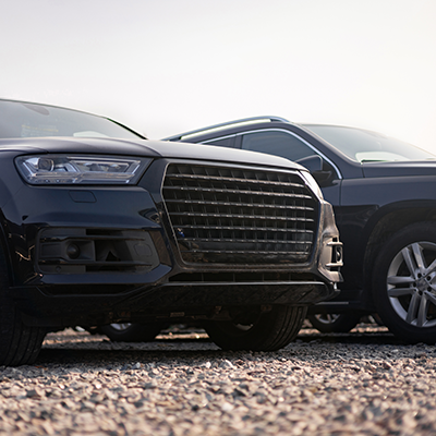 Two Black Suvs Parked Outside On A Gravel Drive