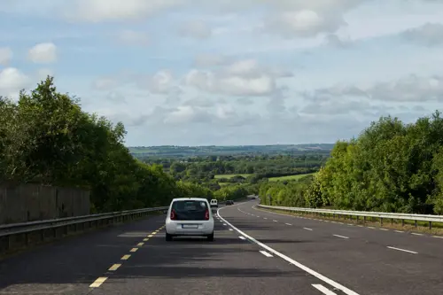 White car driving on Irish highway and countryside on a sunny day