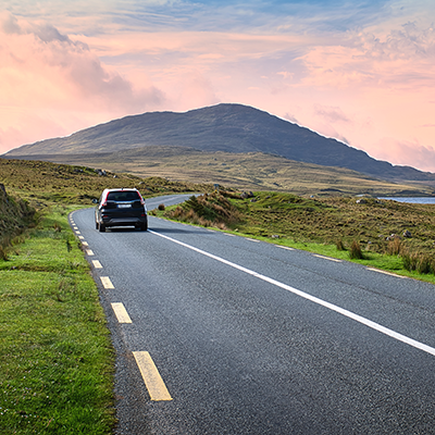 Car Driving On Scenic Country Road In Connemara Ireland With Mountains And Lake At Colorful Sunset Sky
